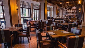 En restaurant med træborde og -stole, store vinduer og hængende plantekasser.