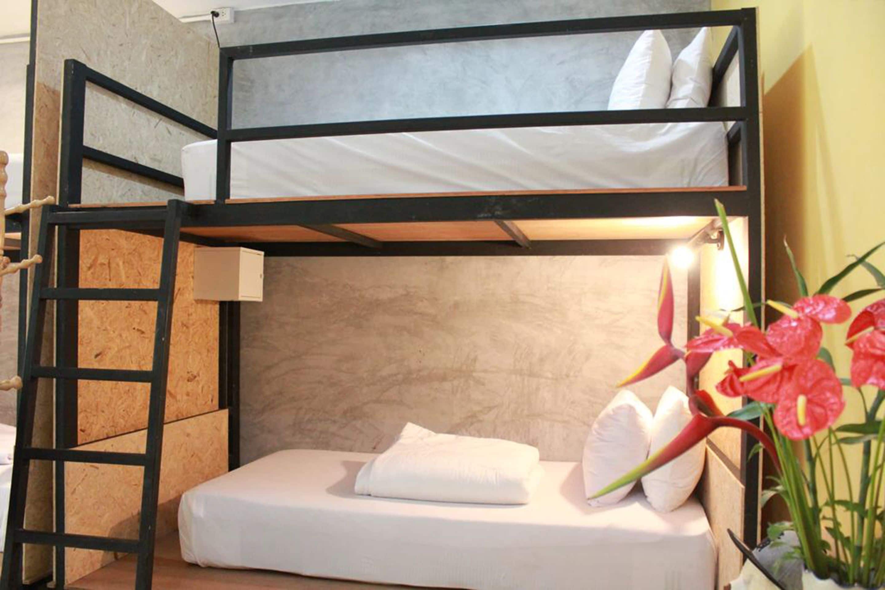 Una cama tipo litera con escalera, una mesita de noche y una maceta con flores rojas.