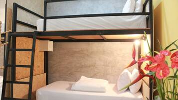 Una cama tipo litera con escalera, una mesita de noche y una maceta con flores rojas.