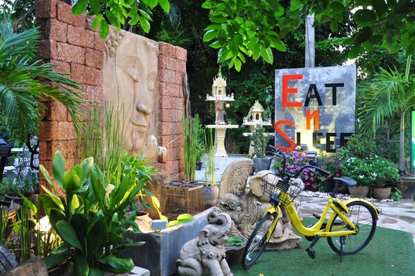 Un jardín con una bicicleta amarilla, esculturas de piedra y un letrero que dice 'EAT HERE'.