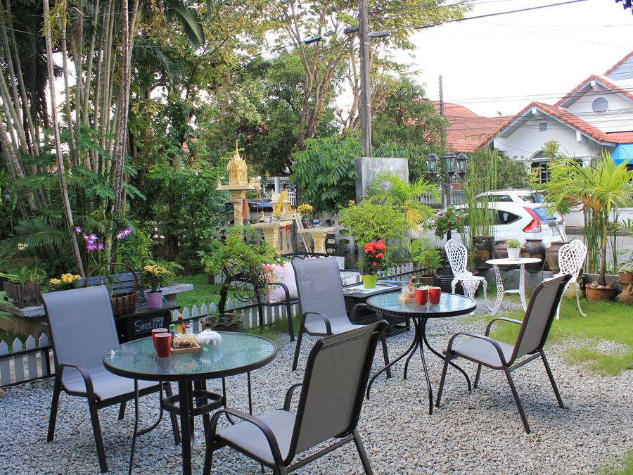 Een buitenpatio met ronde tafels en stoelen, omringd door potplanten en een klein heiligdom.