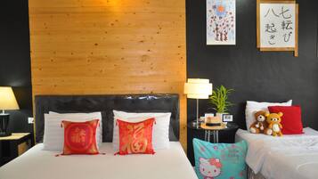 Une chambre d’hôtel avec une tête de lit en bois, deux lits avec des oreillers rouges et blancs, une table de chevet avec une lampe, une petite plante et un coussin à l’effigie de Hello Kitty.