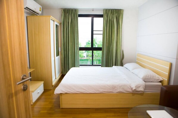A hotel room with a bed, a wardrobe, a desk, and a window with curtains.