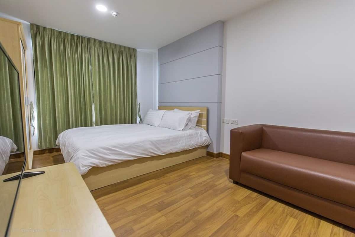 A hotel room with a bed, a brown sofa, a wooden desk, and a green curtain.