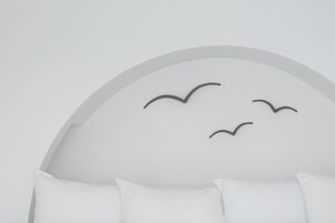 Una habitación moderna con techo blanco curvo y tres almohadas blancas sobre la cama.