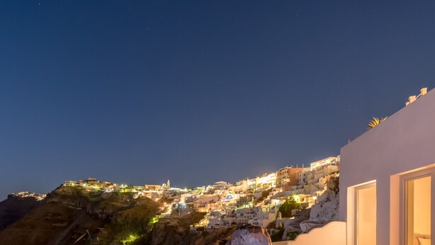 A rooftop terrace with a pool, lounge chairs, and a view of a coastal town at night. - Keti Hotel (Santorini)