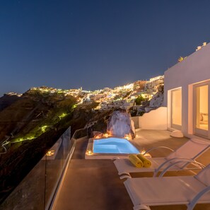 A rooftop terrace with a pool, lounge chairs, and a view of a coastal town at night. - Keti Hotel (Santorini)
