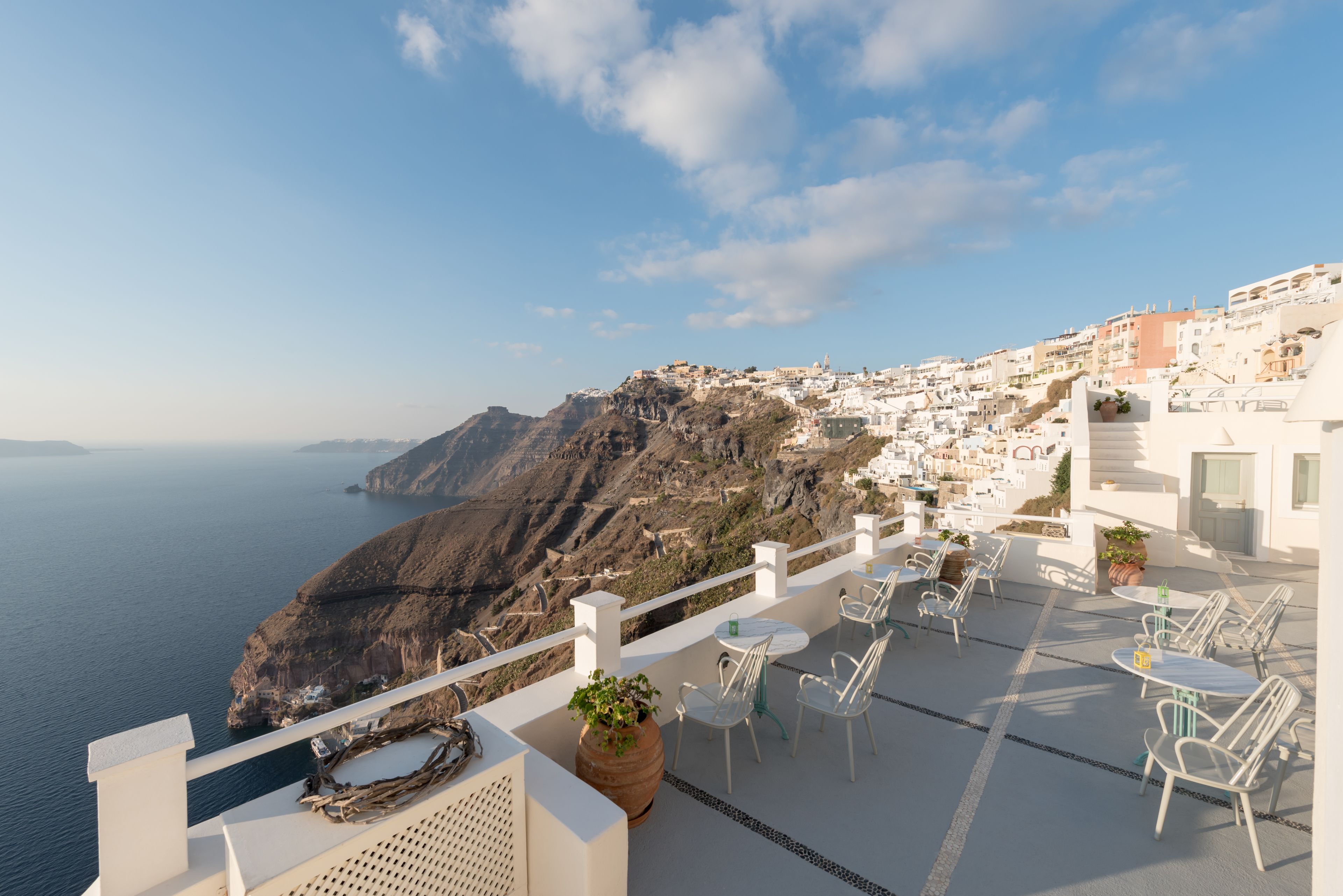 Une terrasse en bord de mer, avec des bâtiments blancs, une vue sur l’océan et une côte rocheuse.