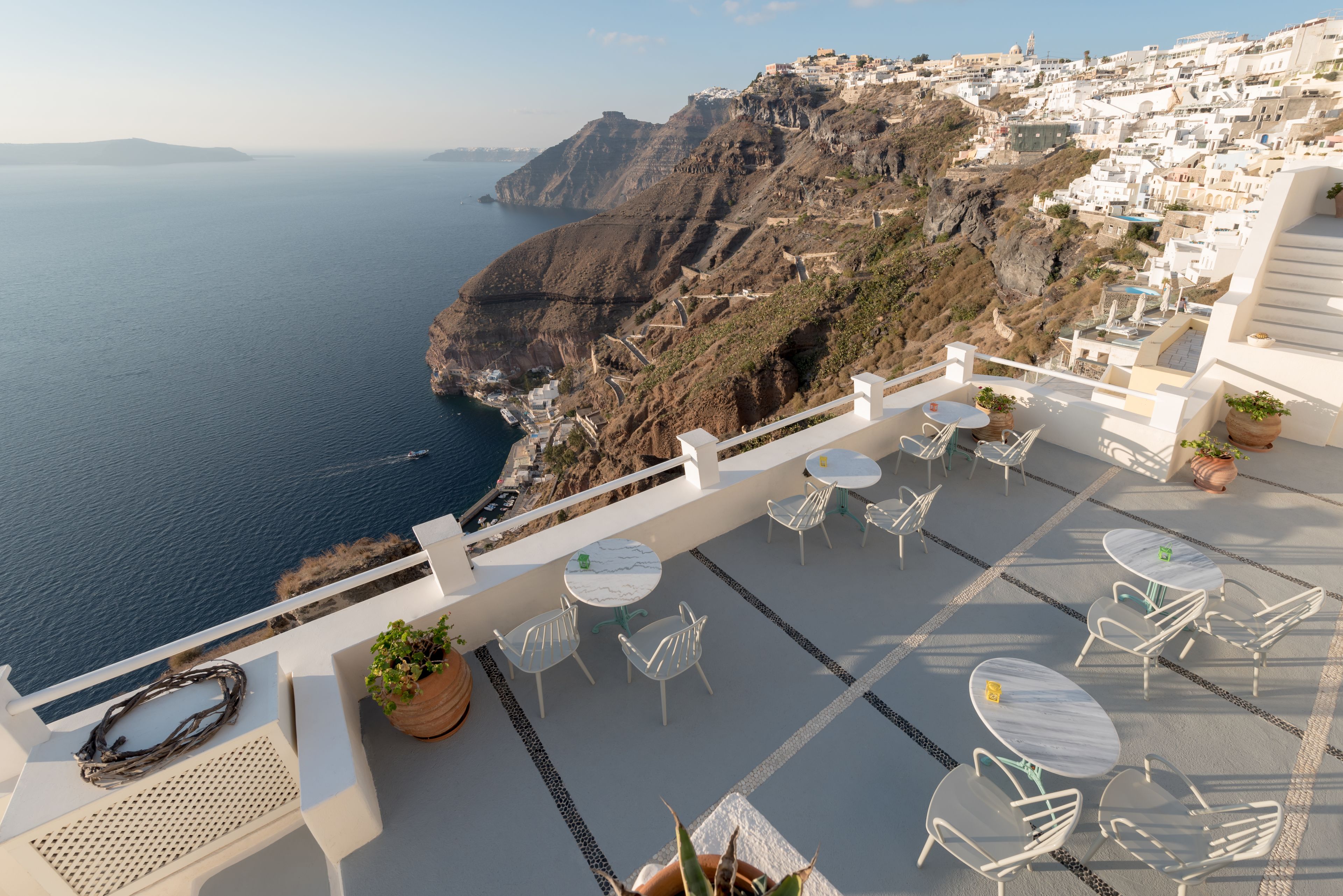 Una terraza con sillas y mesas blancas con vistas a un acantilado costero y al mar.