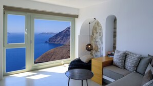 A modern living room with a large window offering a view of the sea and cliffs. - Keti Hotel (Santorini)
