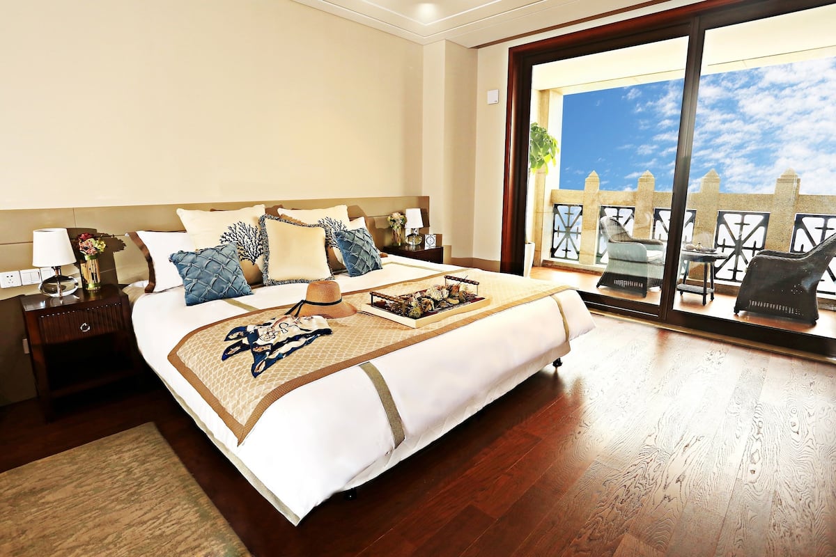 A hotel room with a large bed, a nightstand, a lamp, and a view of the outdoors through a sliding door.
