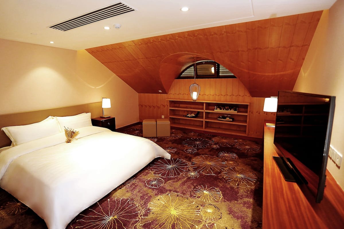 A hotel room with a large bed, a TV, a wooden ceiling, and a decorative carpet.