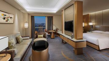 A hotel room with a sofa, a desk, a bed, a TV, and a view of the cityscape.