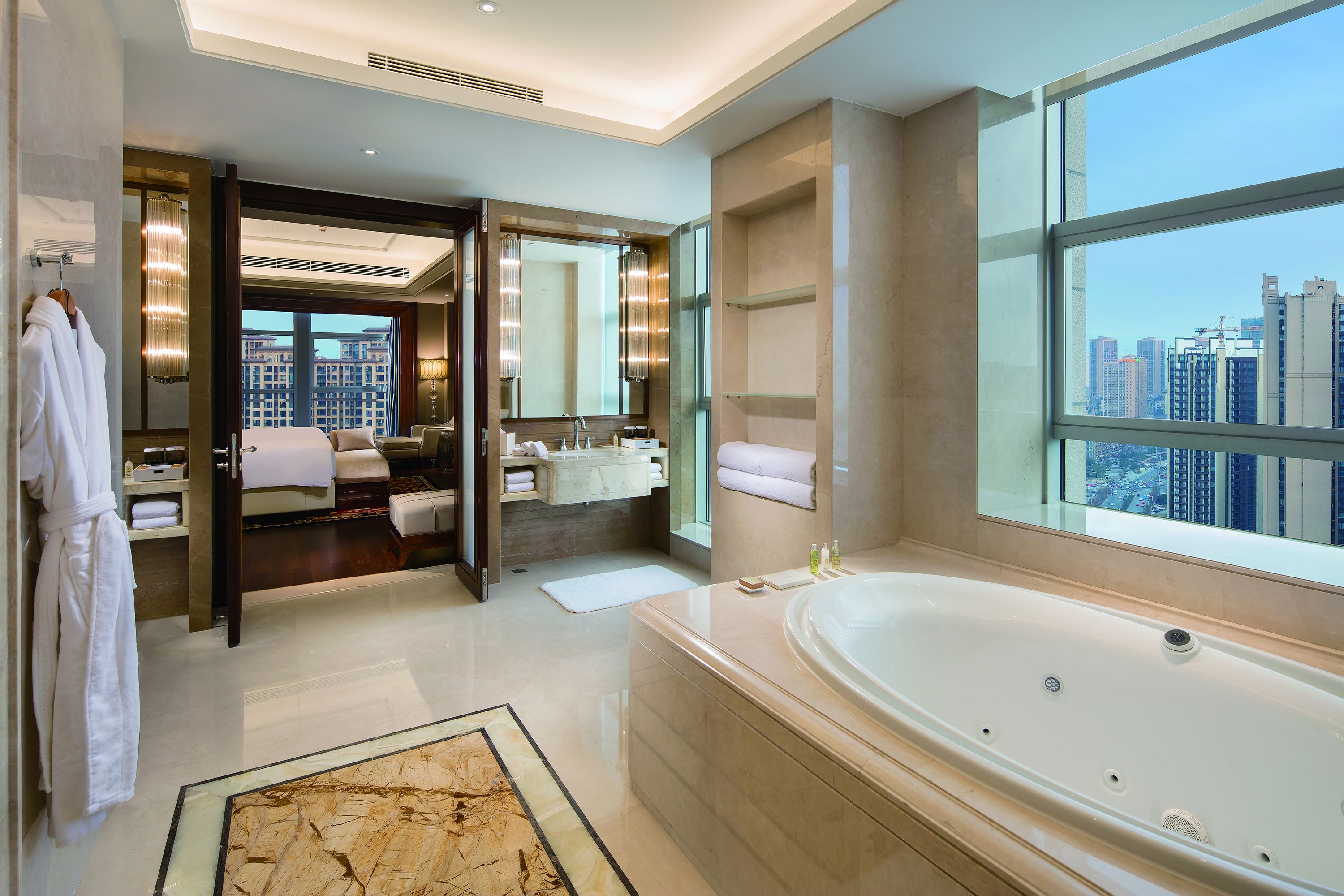 A modern hotel bathroom with a large bathtub, a walk-in shower, and a city view.