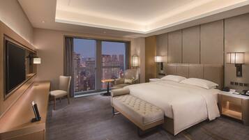 A modern hotel room with a large bed, a desk, a chair, and a TV.
