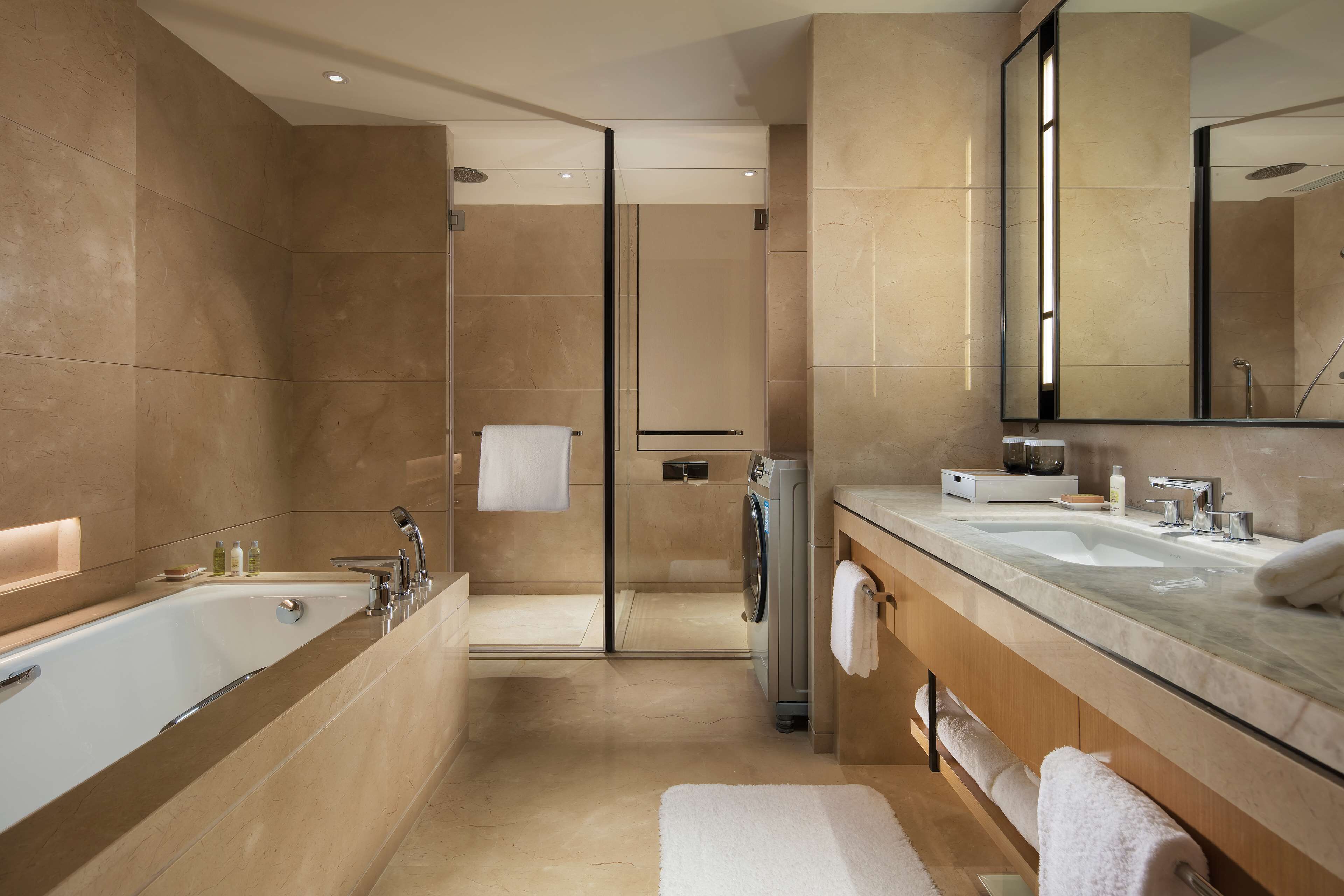 A modern bathroom with a large bathtub, a walk-in shower, and a glass-enclosed toilet.
