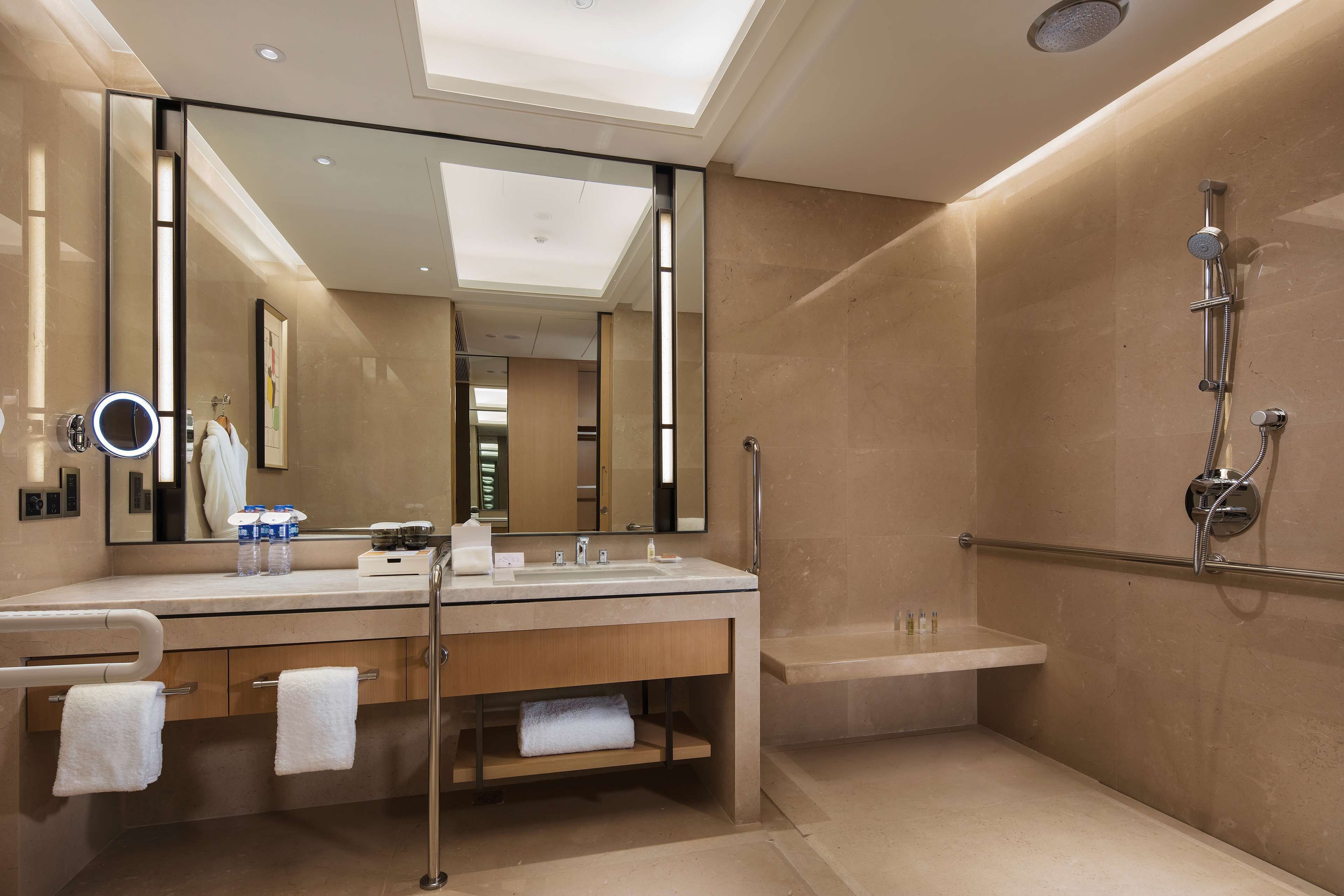 A modern bathroom with a large mirror, a vanity with a sink, a shower with a handheld showerhead, and a towel rack.