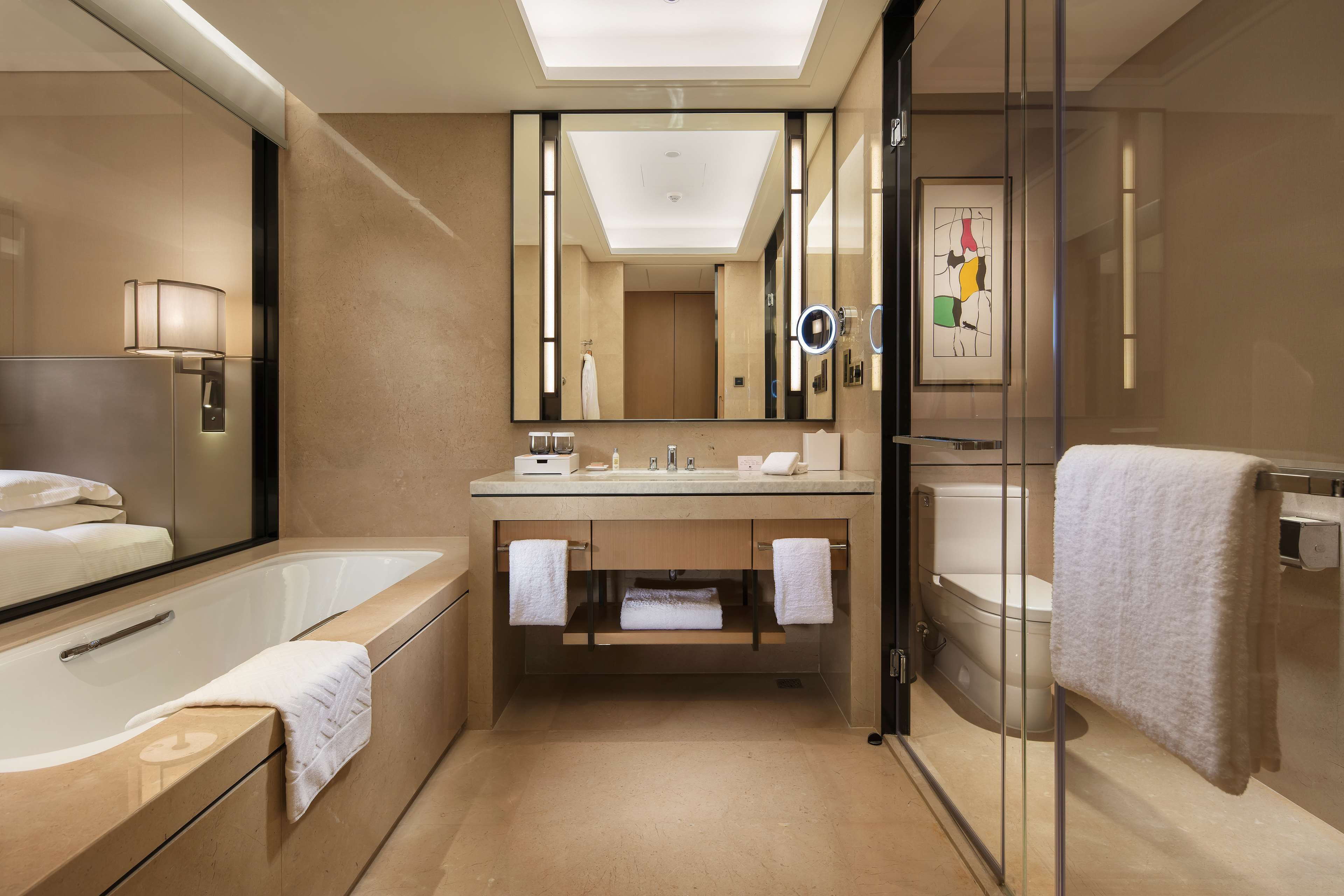A modern bathroom with a large mirror, a bathtub, a toilet, and a sink.