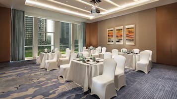 A conference room with round tables, white chairs, and a large window with a view of high-rise buildings.