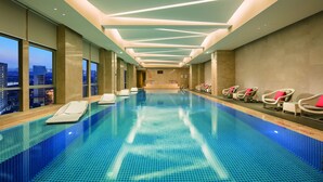 Una piscina interior con vistas a la ciudad, diseño moderno de techo y sillones de descanso a un lado.