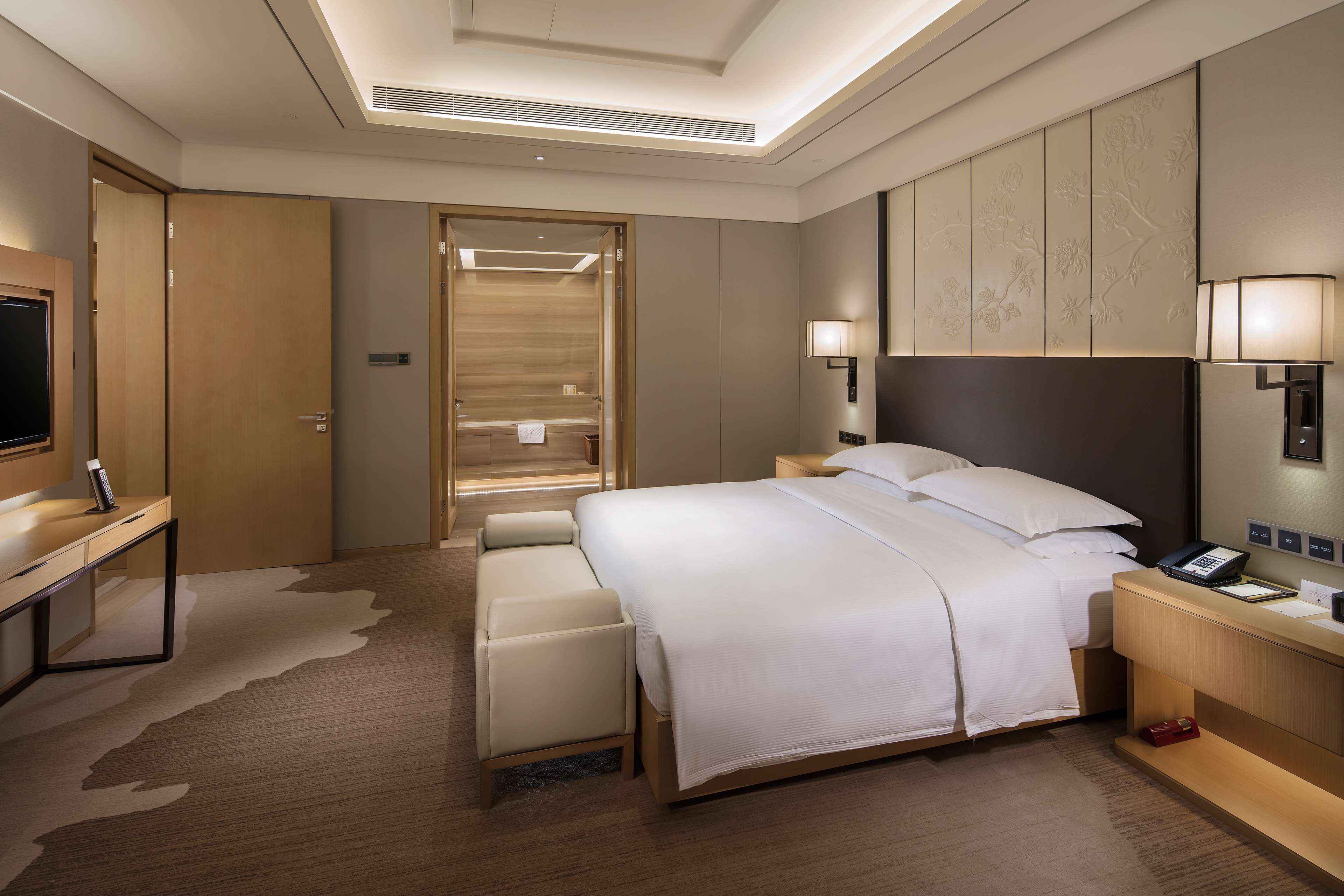 Ein modernes Hotelzimmer mit einem großen Bett, einem Schreibtisch, einem Fernseher und einem Duschbereich.
