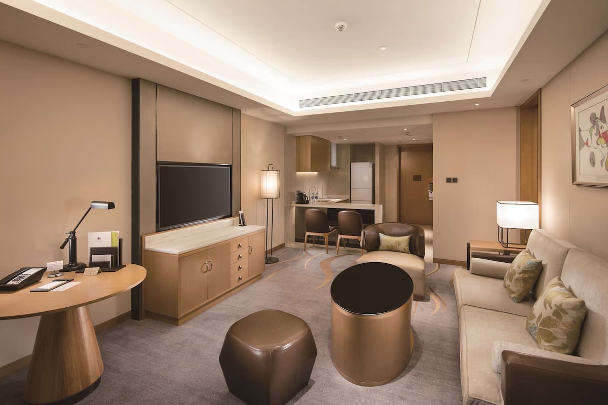 Ett hotellrum med en platt-TV, ett skrivbord med en lampa, en soffa, ett soffbord och en matplats med stolar och ett bord.