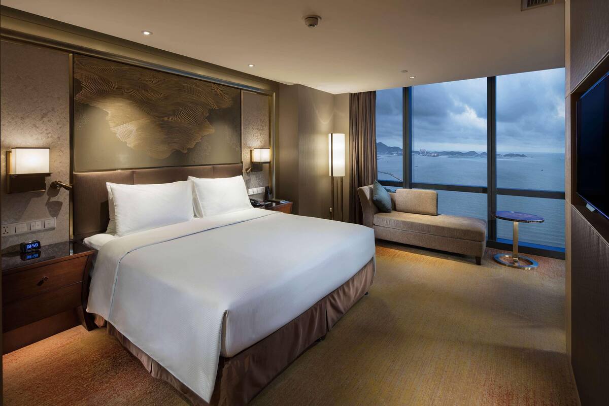 Una habitación de hotel moderna con una cama grande, un sofá, un televisor y vista al mar.