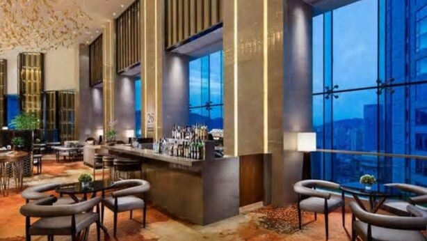 Un moderno vestíbulo de hotel con zona de bar, asientos y amplias ventanas con vistas a la ciudad.