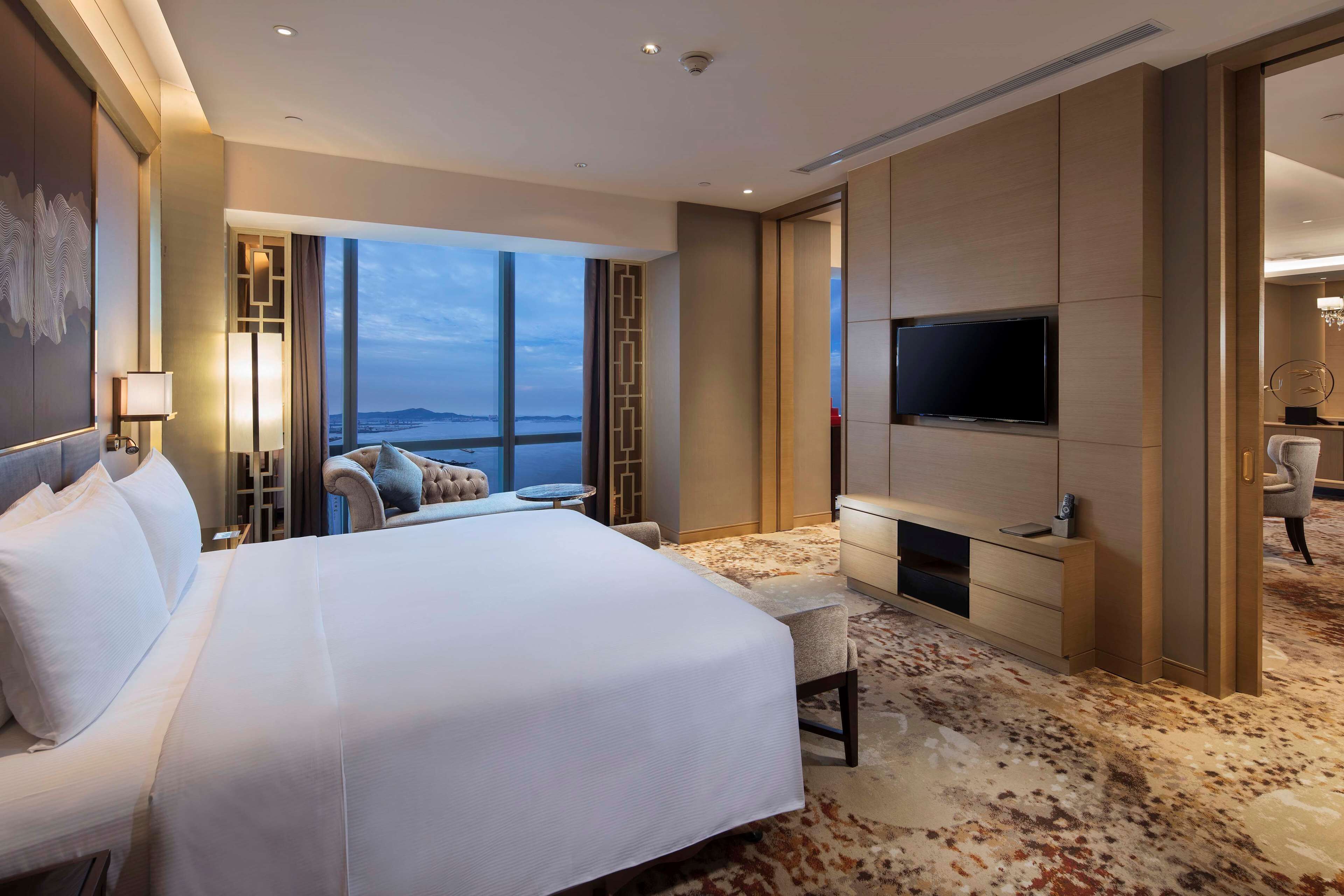 A hotel room with a large bed, a TV, a seating area with a view, and a carpeted floor.