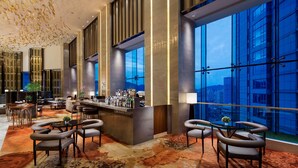 Un moderno vestíbulo de hotel con una zona de bar, arreglos de asientos y ventanas amplias con vista a la ciudad.