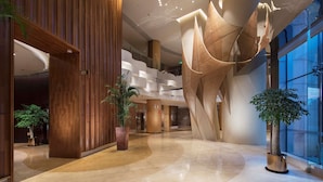 Un vestíbulo moderno con una gran escultura abstracta, paneles de madera y plantas en macetas.