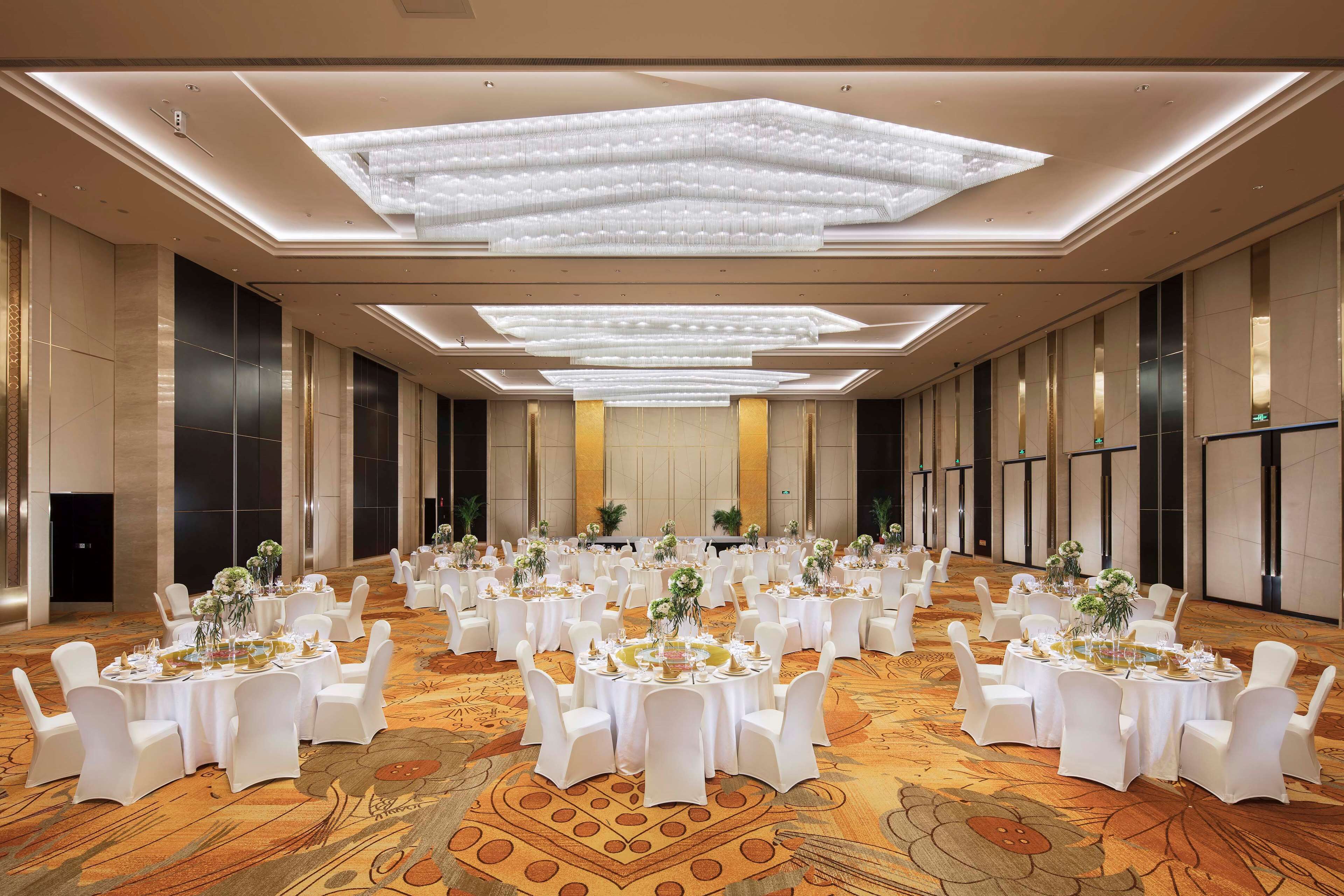 A large banquet hall with round tables, white chairs, and floral centerpieces.