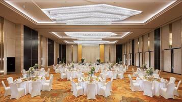 A large banquet hall with round tables, white chairs, and floral centerpieces.