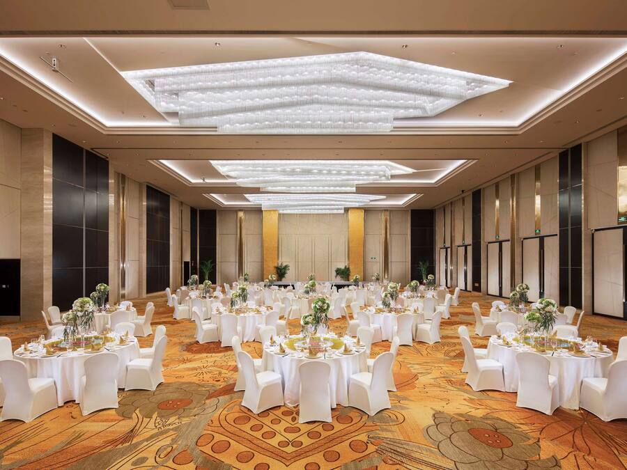 A large banquet hall with round tables, white chairs, and floral centerpieces.