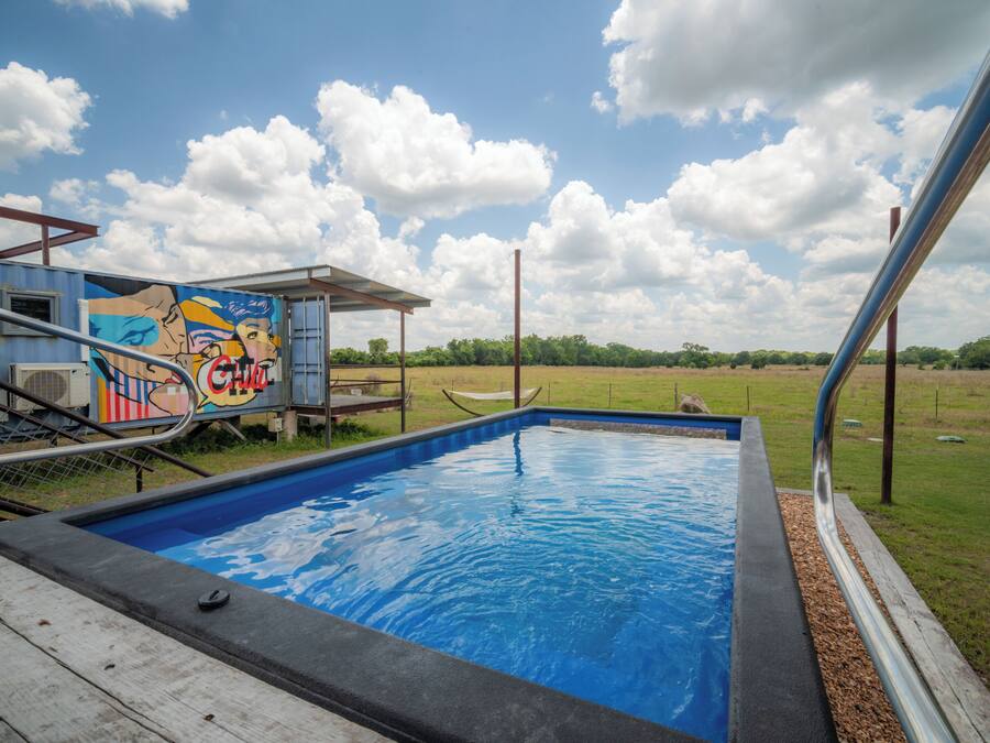 A swimming pool with a view of a grassy field and a mural on a building.