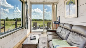 A cozy room with a leather sofa, a small table, and a window overlooking a grassy field. - Flophouze Shipping Container Hotel (Round Top)
