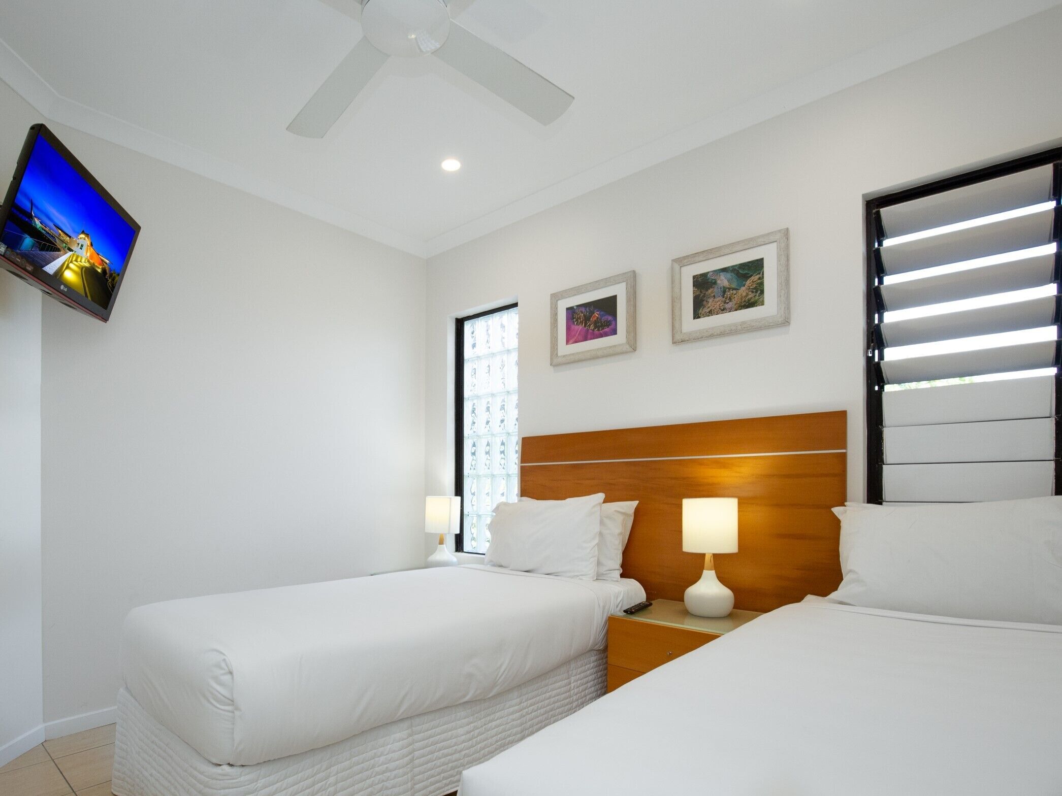 A hotel room with two beds, a TV mounted on the wall, and two framed pictures above the beds.