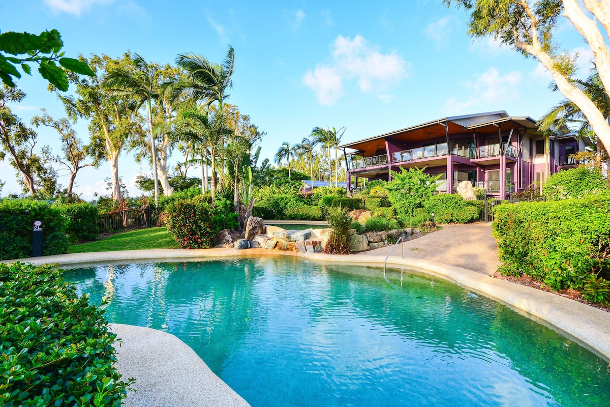 A modern building with a pool surrounded by lush greenery and palm trees.