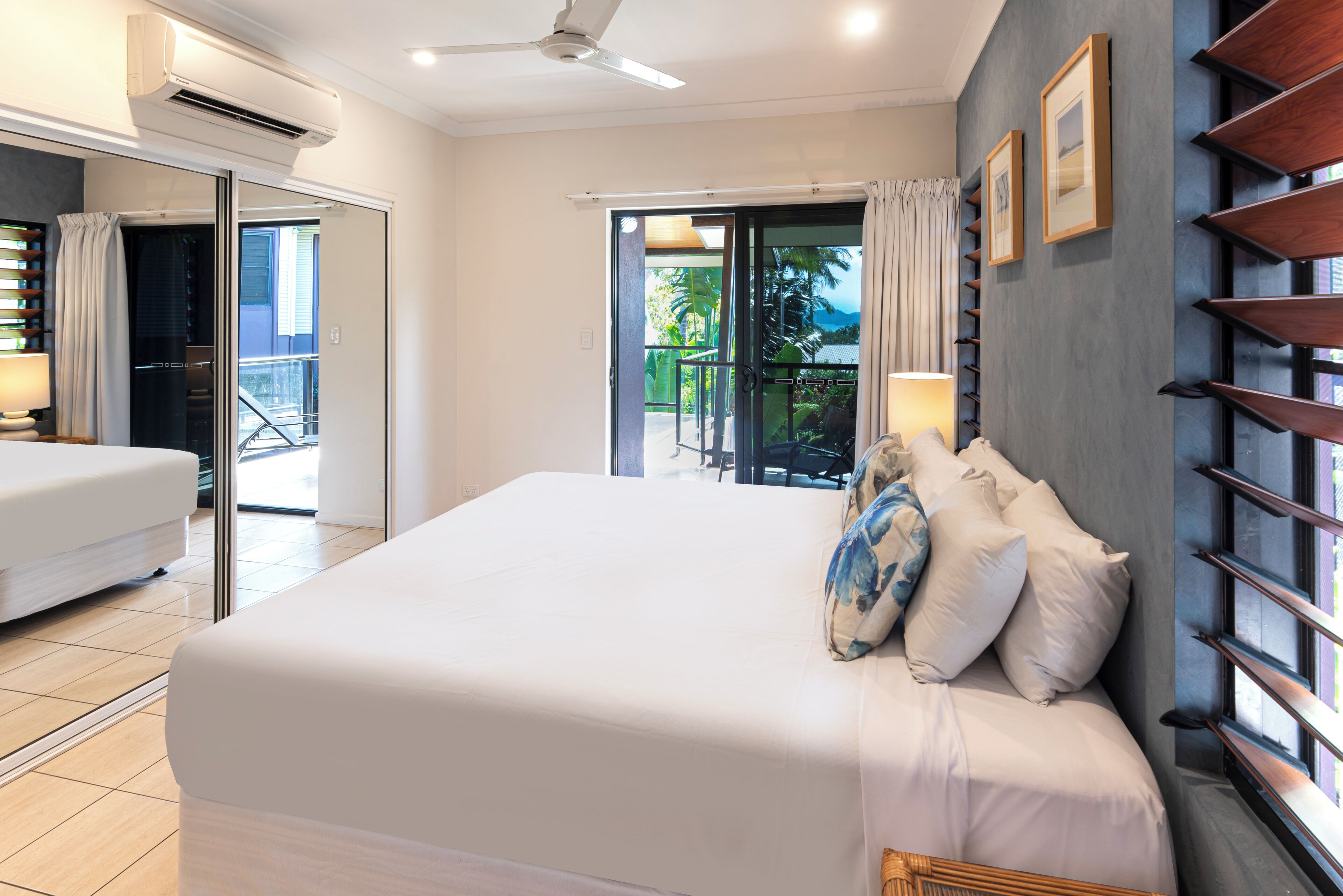 A hotel room with a large bed, a balcony with a view, and a ceiling fan.