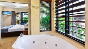 Ein modernes Badezimmer mit einer großen Badewanne, ein Bett mit Blick ins Freie und ein Fernseher an der Wand.