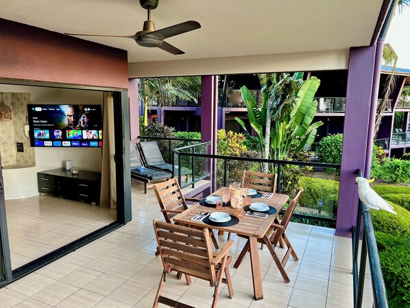 A dining area with a table set for four, a ceiling fan, and a TV displaying a movie.