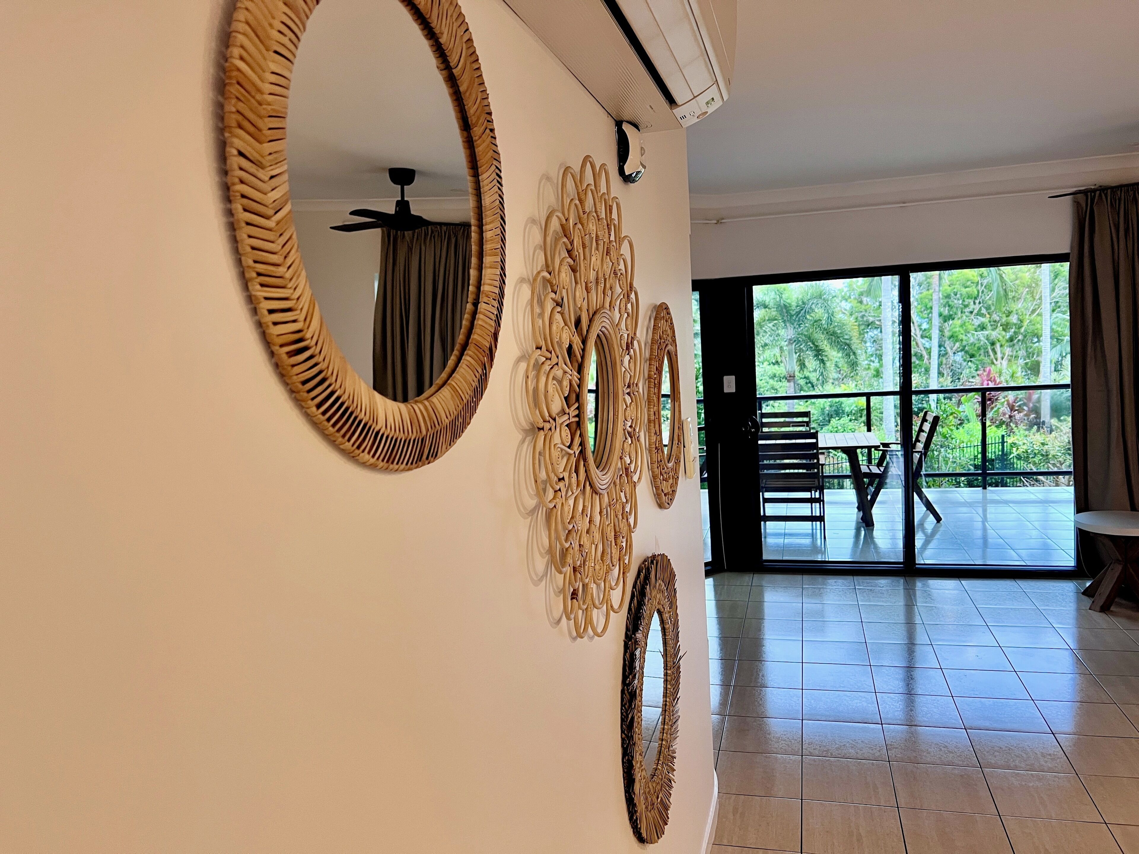 A room with a large mirror, a ceiling fan, and a view of an outdoor patio with a table and chairs.