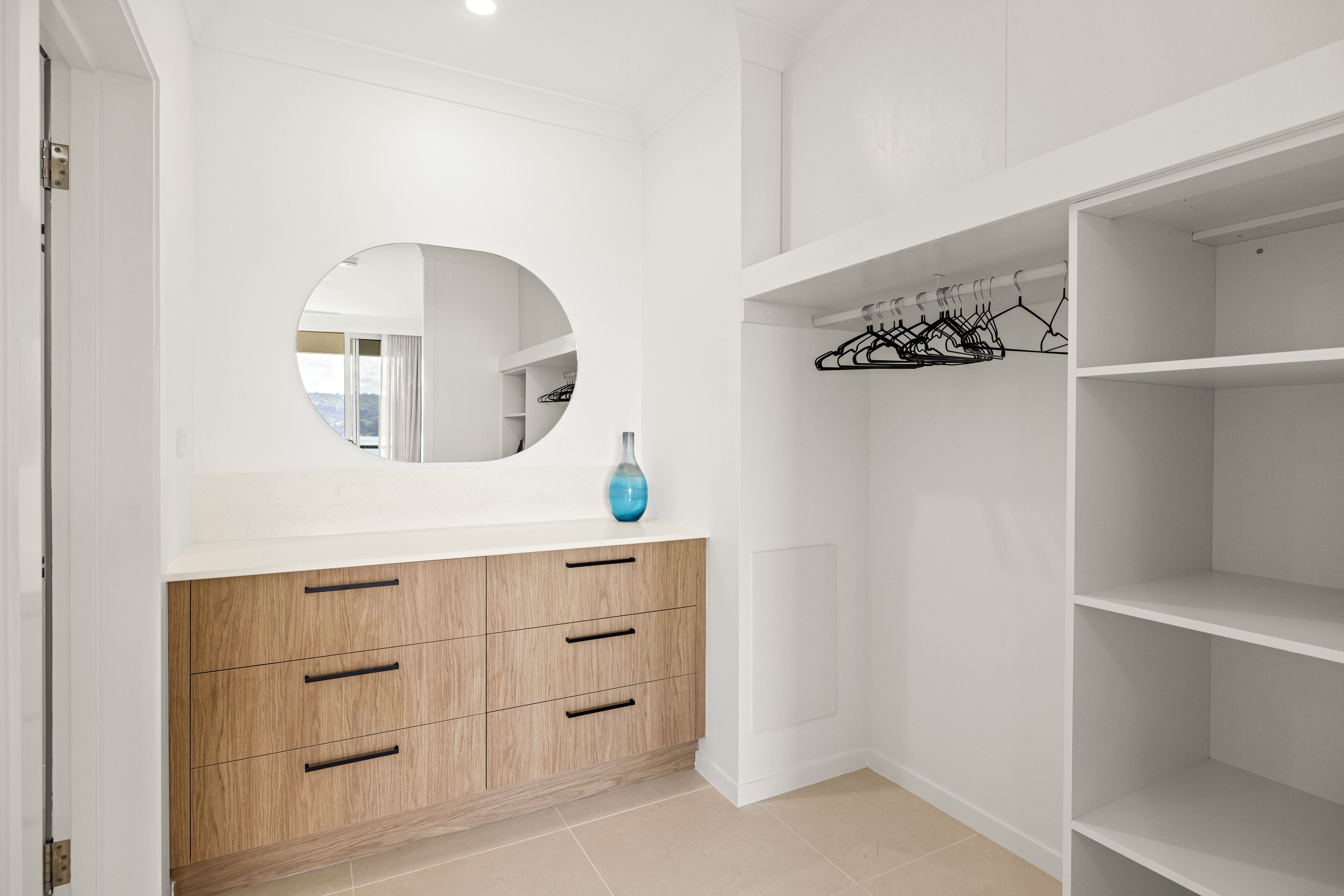 A modern closet with a mirror, wooden drawers, and a hanging rack.