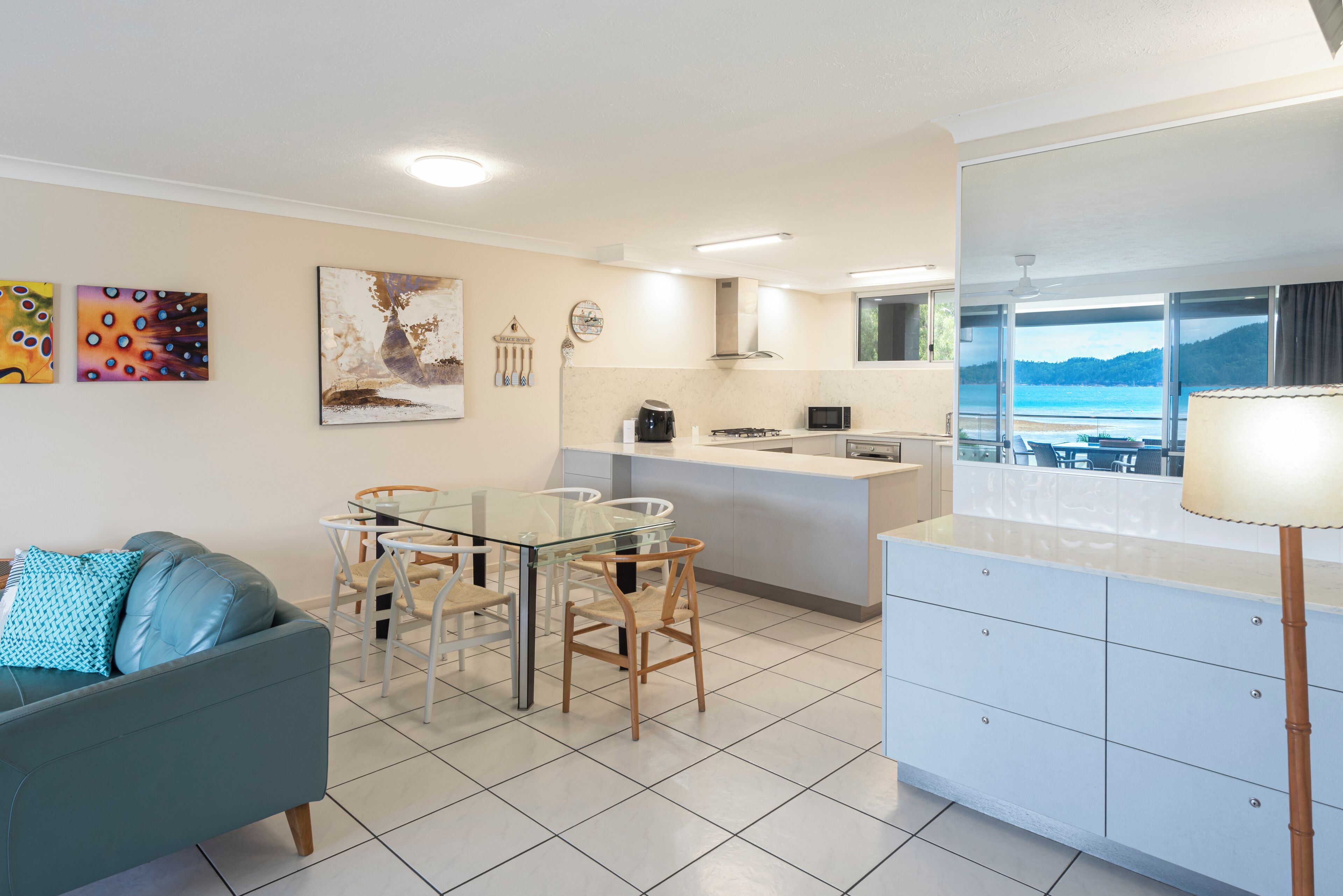 A modern kitchen with a dining area, a sofa, and a view of the sea.