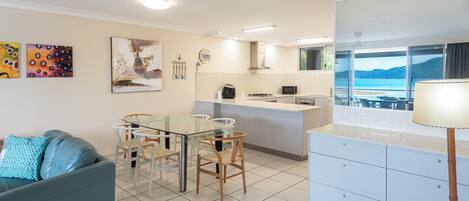 A modern kitchen with a dining area, a sofa, and a view of the sea.