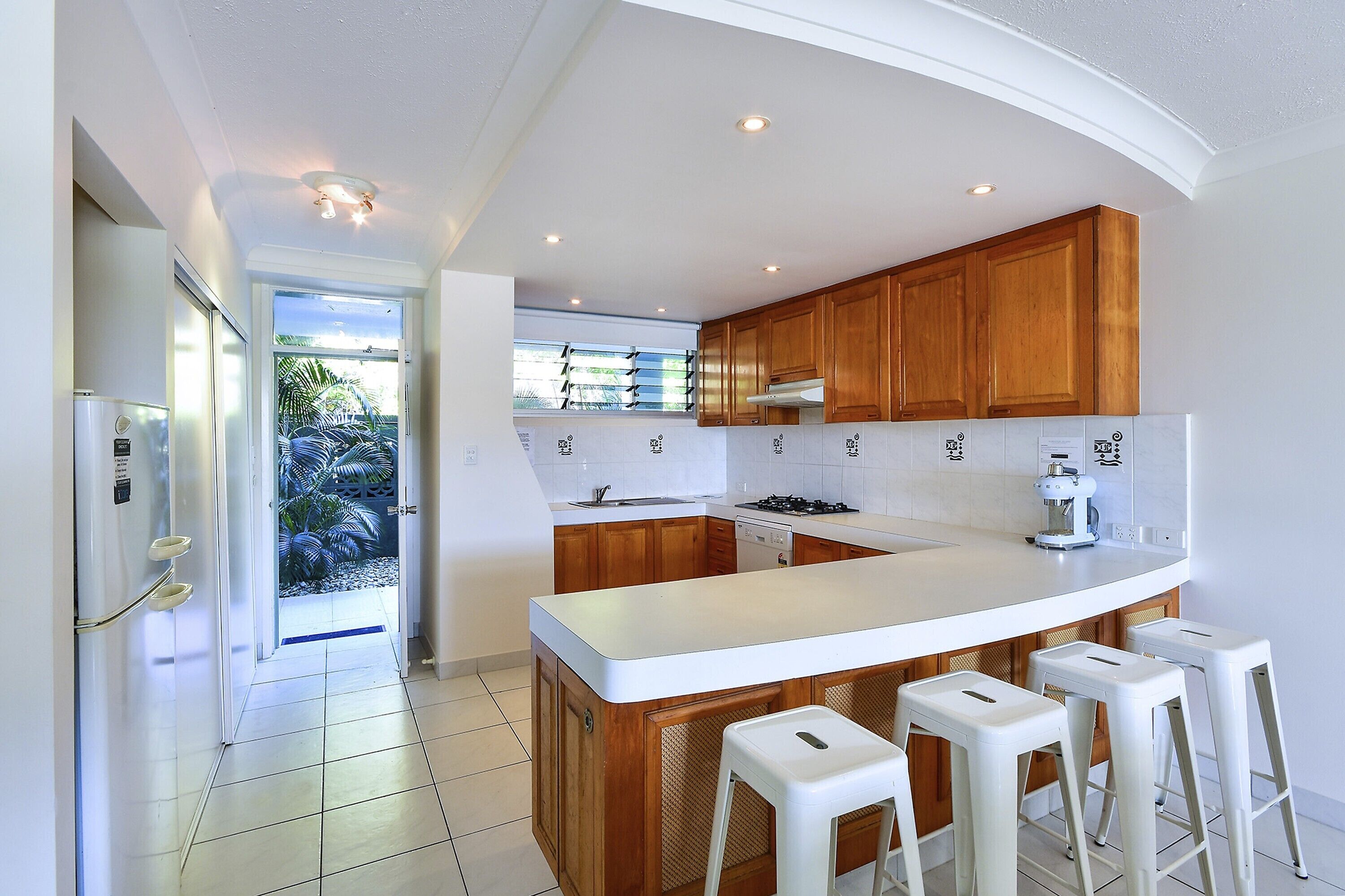 A modern kitchen with wooden cabinets, a white countertop, and a built-in island with bar stools.