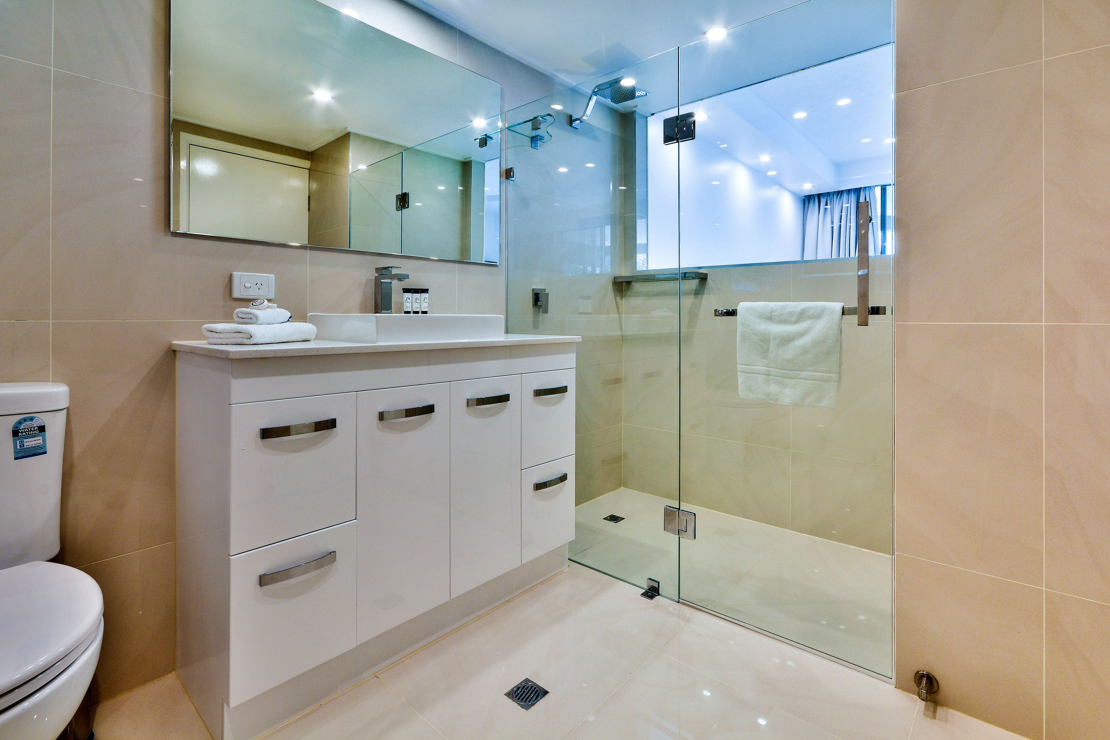 A modern bathroom with a glass-enclosed shower, a white vanity with drawers, and a large mirror above the sink.