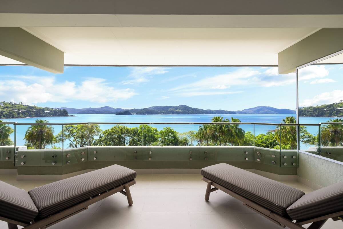 Un balcon avec deux fauteuils de jardin, une vue dégagée sur un lac et des montagnes, et une balustrade en verre.