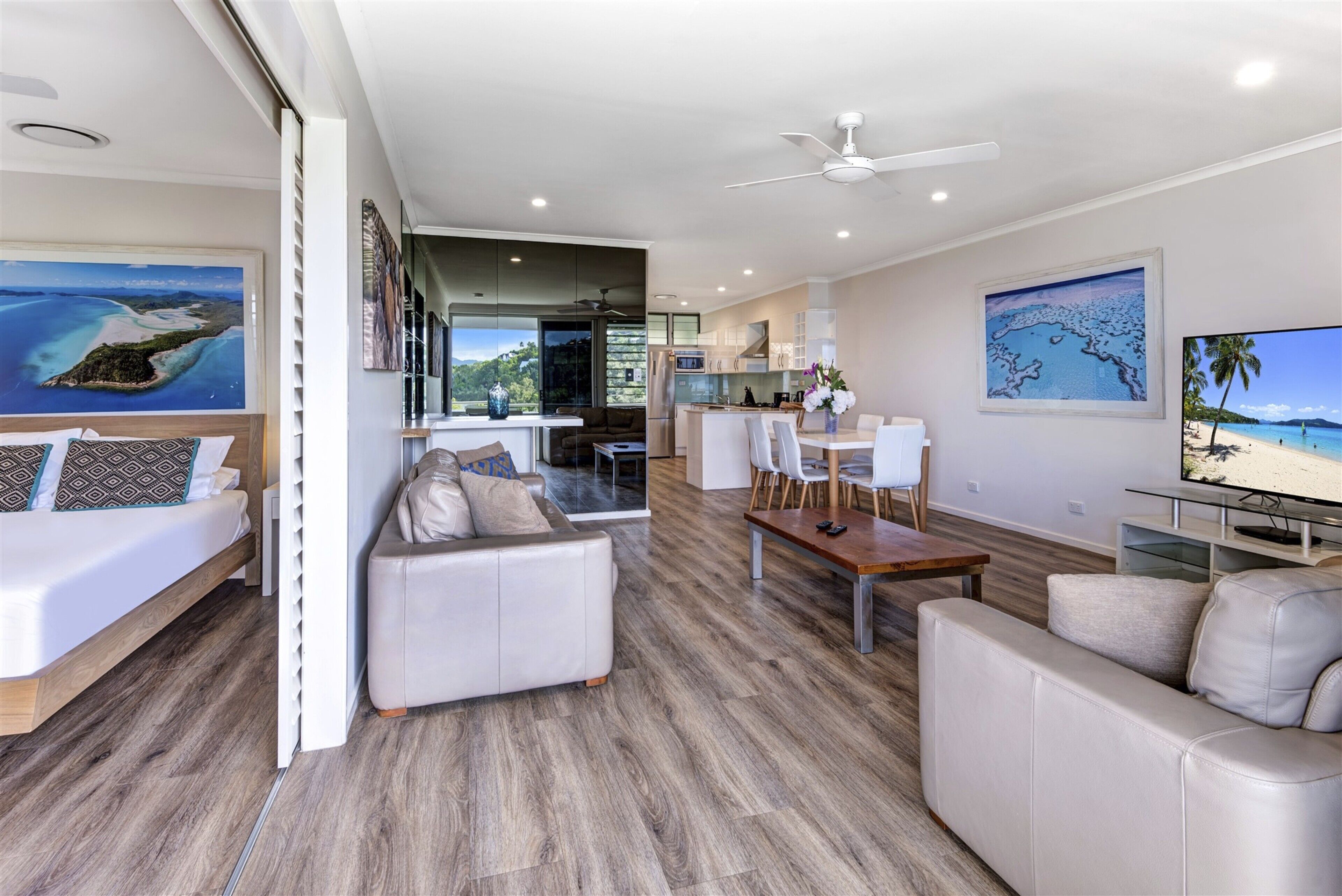 A modern living room with a sofa, a dining table, and a kitchen area visible through an open door.
