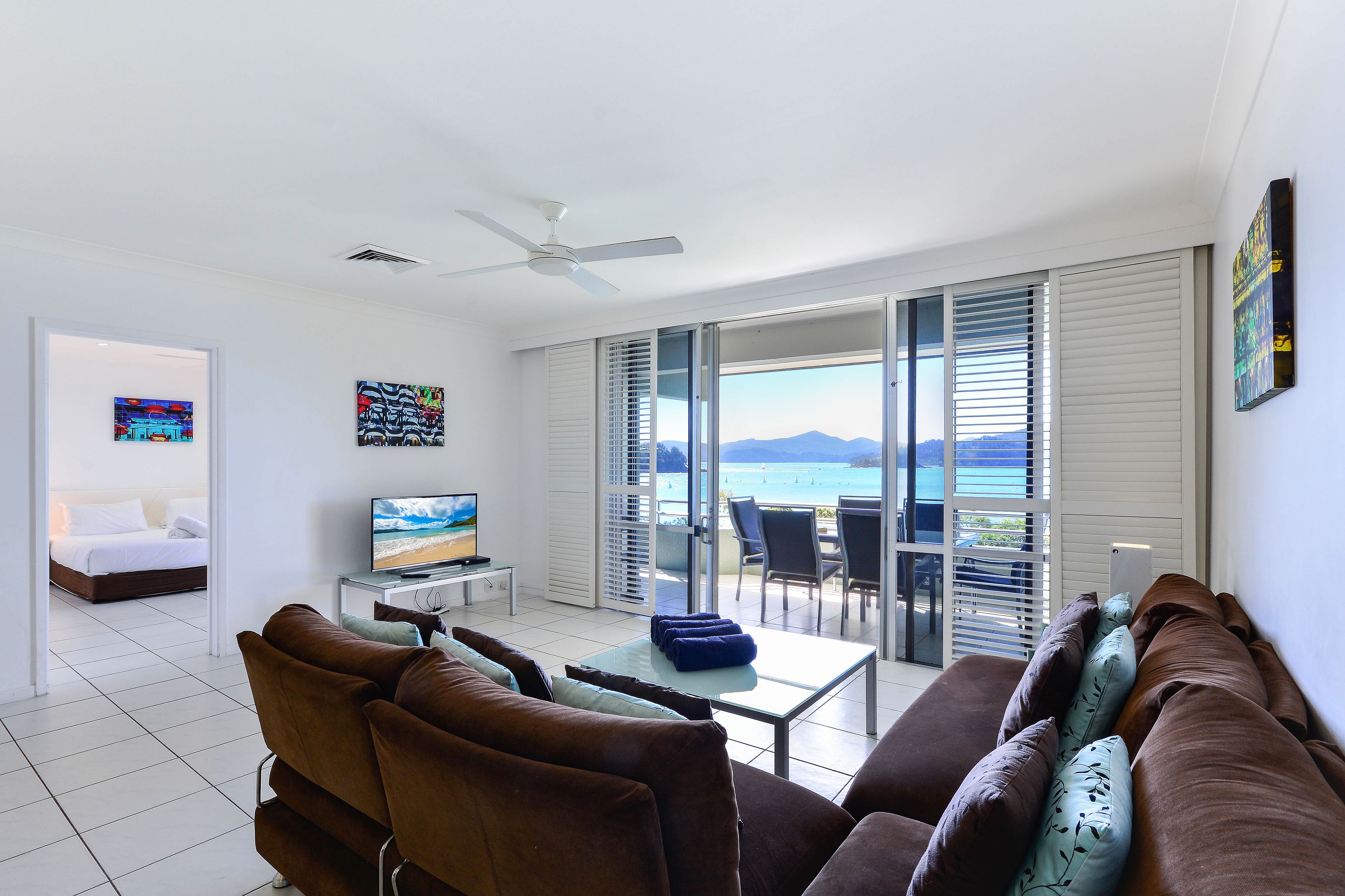 Un salon moderne avec un canapé, une table basse et un téléviseur. Il y a un balcon avec vue sur la mer.